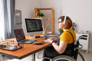 Smart disabled coder sitting in wheelchair and using computers while working from home